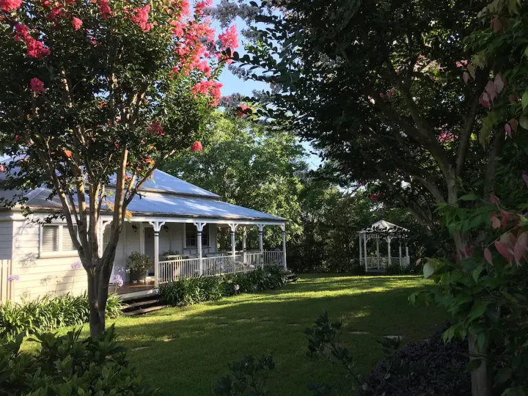 Dovecote Cottage, a white Queenslander with a veranda, in the farm gardens