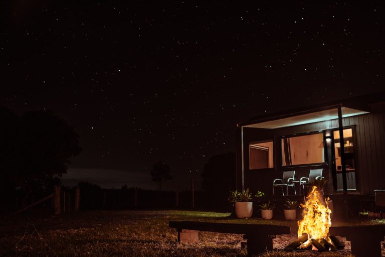 The tiny house at night with the outdoor fire lit under a starry sky